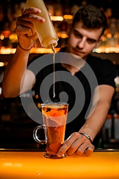 bartender adds syrup to tea with lemon slices in transparent cup on the bar