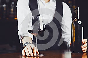 Bartender at the bar with a glass of red wine and bottle, close-up.