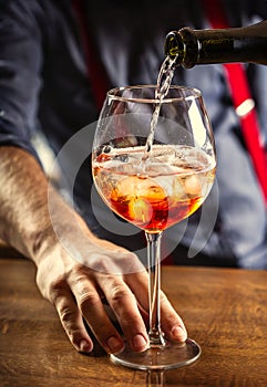 The bartender at the bar prepares the summer cocktail Spritz Veneziano, pours Prosecco into a glass with ice