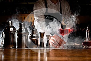Bartender in black apron holding red tasty alcoholic cocktail
