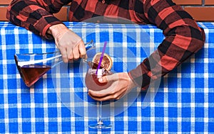 Bartender concept. Male hands holding bottle, pouring glass, making alcoholic cocktail. Man in checkered shirt, faceless