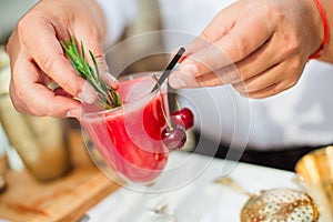The bartender decorates a summer red cocktail with a sprig of rosemary. Daylight.
