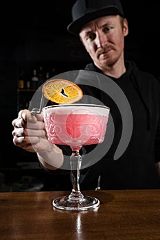 Bartender is decorating pink Clover club alcoholic cocktail with orange slice at the bar. Bartender mixes egg white