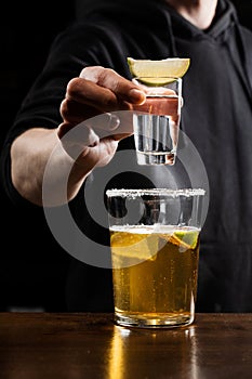 Bartender drops shot of tequila with lime into beer glass. Alcoholic cocktail Death of Mexican on black background.