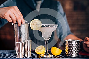 Bartender garnishing drink, pouring lime margarita in fancy glass at restaurant