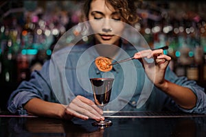 Bartender girl adding a dried tomato with tweezers to a cocktail glass with alcoholic drink