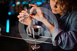 Bartender girl adding a glitter from the brush to a cocktail glass with alcoholic drink