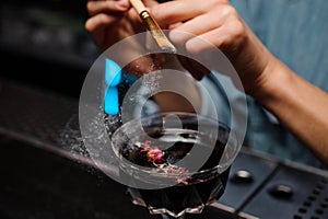 Bartender girl adding a glitter from the brush to a cocktail glass with alcoholic drink decorated with rose petals