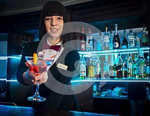 Bartender girl at night club counter offering coctail b