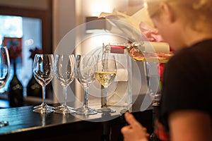 Bartender girl pours white wine into glasses. Restaurant bar, wine party.