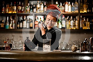 Bartender girl with a red dreadlocks pouring a alcoholic drink from the jigger to a measuring glass cup