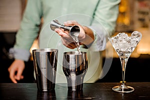 Bartender hands pouring drink into a jigger to prepare a cocktail close up