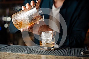 Bartender hands pouring fresh summer alcoholic cocktail into a glass