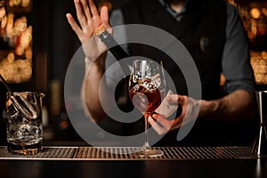 Bartender holding a bottle on the foreground of glass with a cocktail