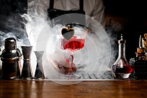 Bartender holding decorated red tasty alcohol cocktail in small glass