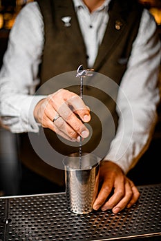 bartender holding long bar spoon and stirring cocktail in steel mixing cup