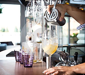 Bartender holding steel shaker up and pouring mixed drink into t