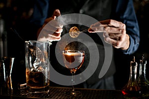 Bartender holds tweezers with slice of citrus over glass and sprinkles on it.