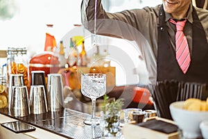 Bartender mixing a cocktail in a crystal glass in an american bar - Barman pouring alcohol in a glass with aromatic herbs