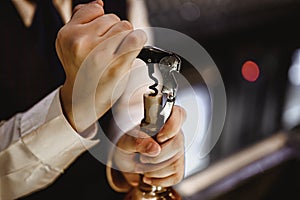 The bartender opens a bottle of red wine using a wine opener.