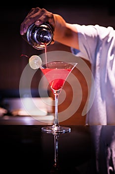 Bartender pour Red Martini cocktail into a glass with slice of l