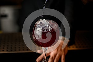 Bartender pouring alcohol cocktail in glass with ice