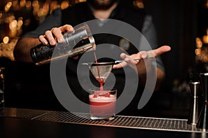 Bartender pouring alcohol drink using shaker and sieve