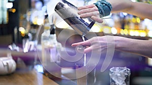 Bartender pouring alcohol through a strainer, bar counter background