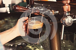 Bartender pouring beer from tap into glass in bar