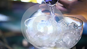 Bartender pouring cocktail into a glass with ice, macro shot