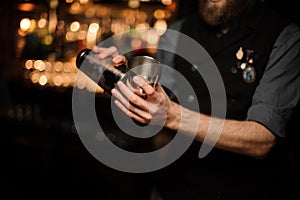Bartender pouring cocktail with in a steel shaker