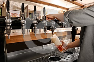 Bartender pouring fresh beer into glass in pub, closeup