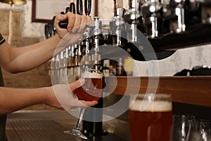 Bartender pouring fresh beer into glass in pub