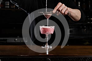 Bartender is pouring pink Clover club alcoholic cocktail in the glass. Bartender mixes egg white, lemon, dry vermouth