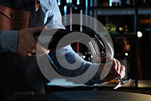 Bartender pouring red wine from bottle into glass indoors, closeup