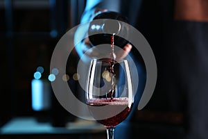 Bartender pouring red wine from bottle into glass indoors, closeup