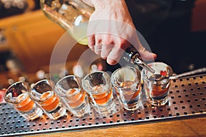 Bartender pouring strong alcoholic drink into small glasses on bar, shots.