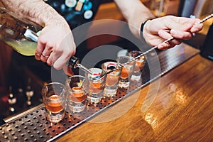 Bartender pouring strong alcoholic drink into small glasses on bar, shots.