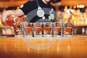 Bartender pouring strong alcoholic drink into small glasses on bar, shots.