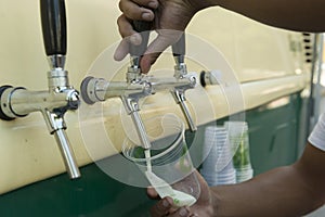 Bartender pouring from tap fresh beer into the plastic cup