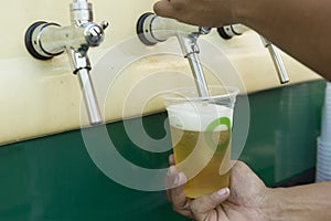 Bartender pouring from tap fresh beer into the plastic cup