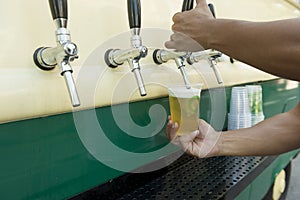 Bartender pouring from tap fresh beer into the plastic cup