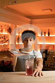 Bartender pouring tonic water in alcoholic cocktail in glass on bar counter