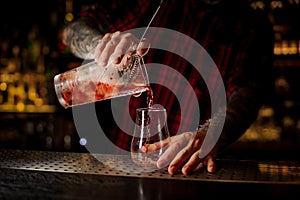 Bartender pourring a red Sazerac cocktail from the measuring cup