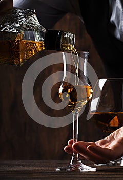 The bartender pours the grappa or liquor in small shot glass on the old bar counter. Vintage wooden background in pub or bar,