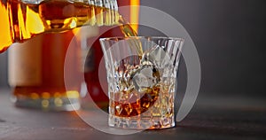 bartender pours whiskey into glass with cold iron cubes for cooling on a background of bottles