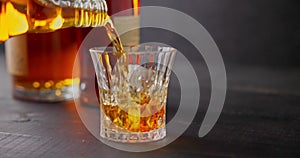 bartender pours whiskey into glass with ice cubes for cooling on a background of bottles