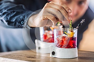 Bartender precisely preparing cocktail drink with fruit and herb decoration. Bartender only hands preparing alcoholic drink.