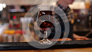 The bartender puts a ball of ice cream on a cocktail with cola and ice, close-up