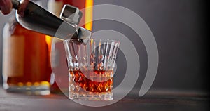 bartender puts cold iron cubes for cooling into a glass of whiskey on a background of bottles